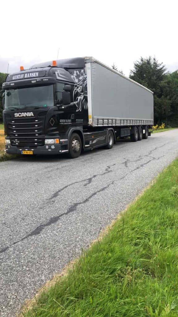 Sort Scania lastbil med hvid lukket trailer svinger ind på en asfalteret vej.