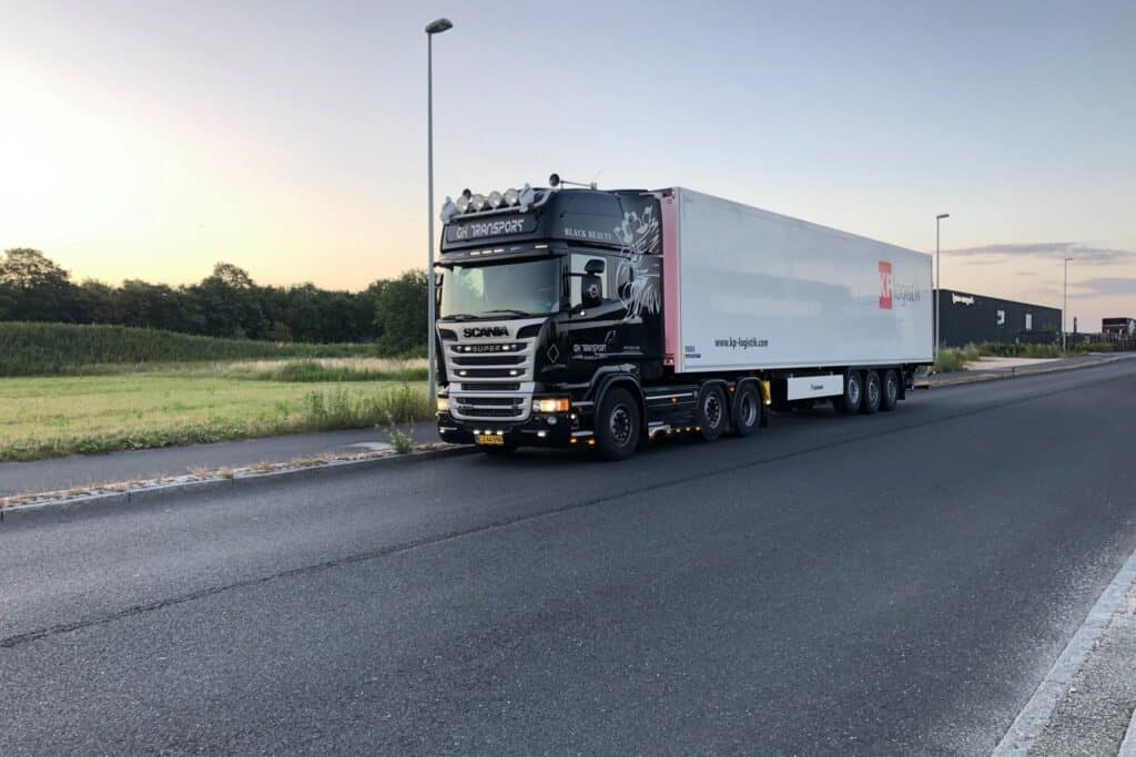 Sort lastbil med stor hvid bokstrailer fra Gustav Hansen holder på en landevej.