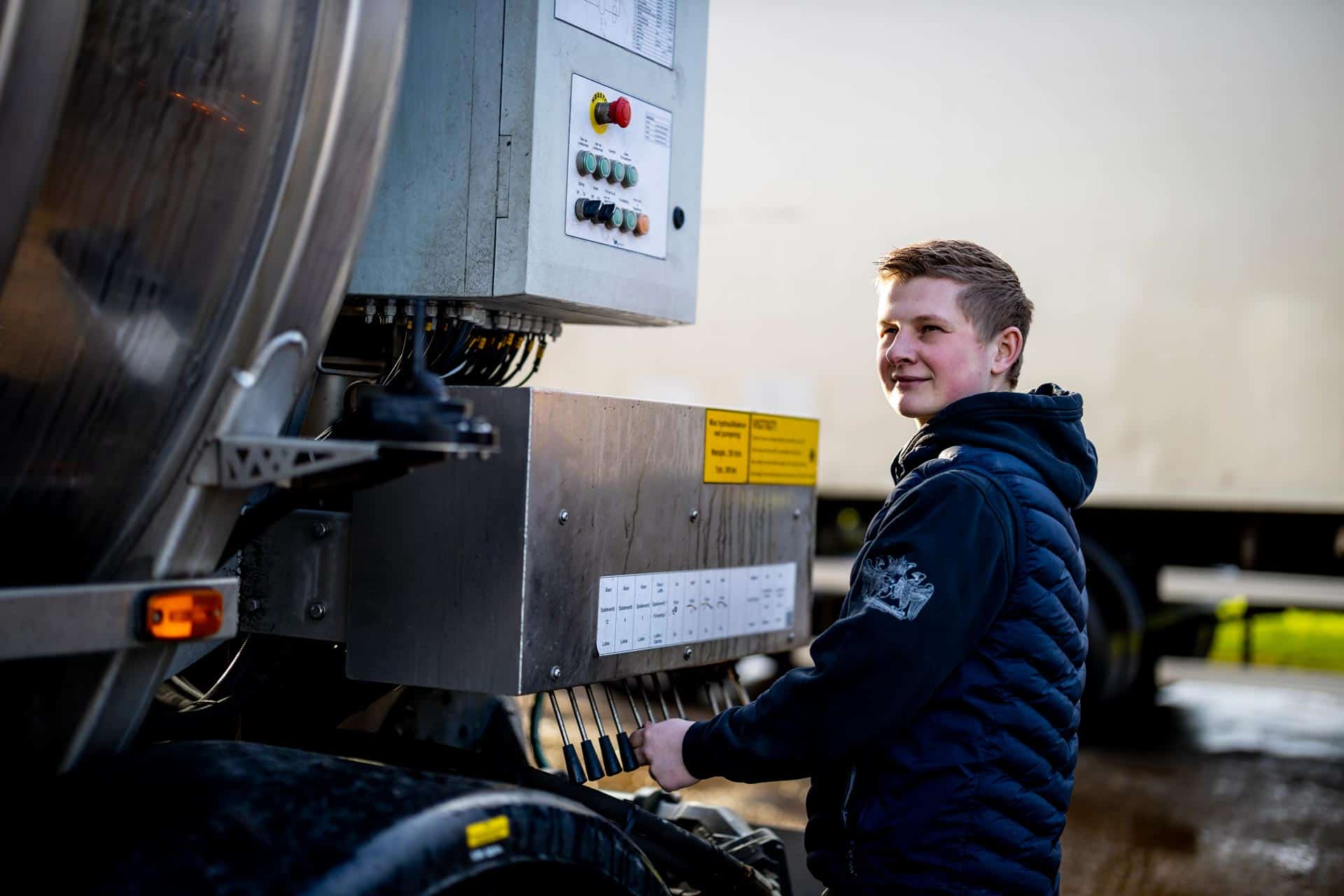 Smilende chauffør står ved bagsmækken af en stor trailer fra Gustav Hansen.