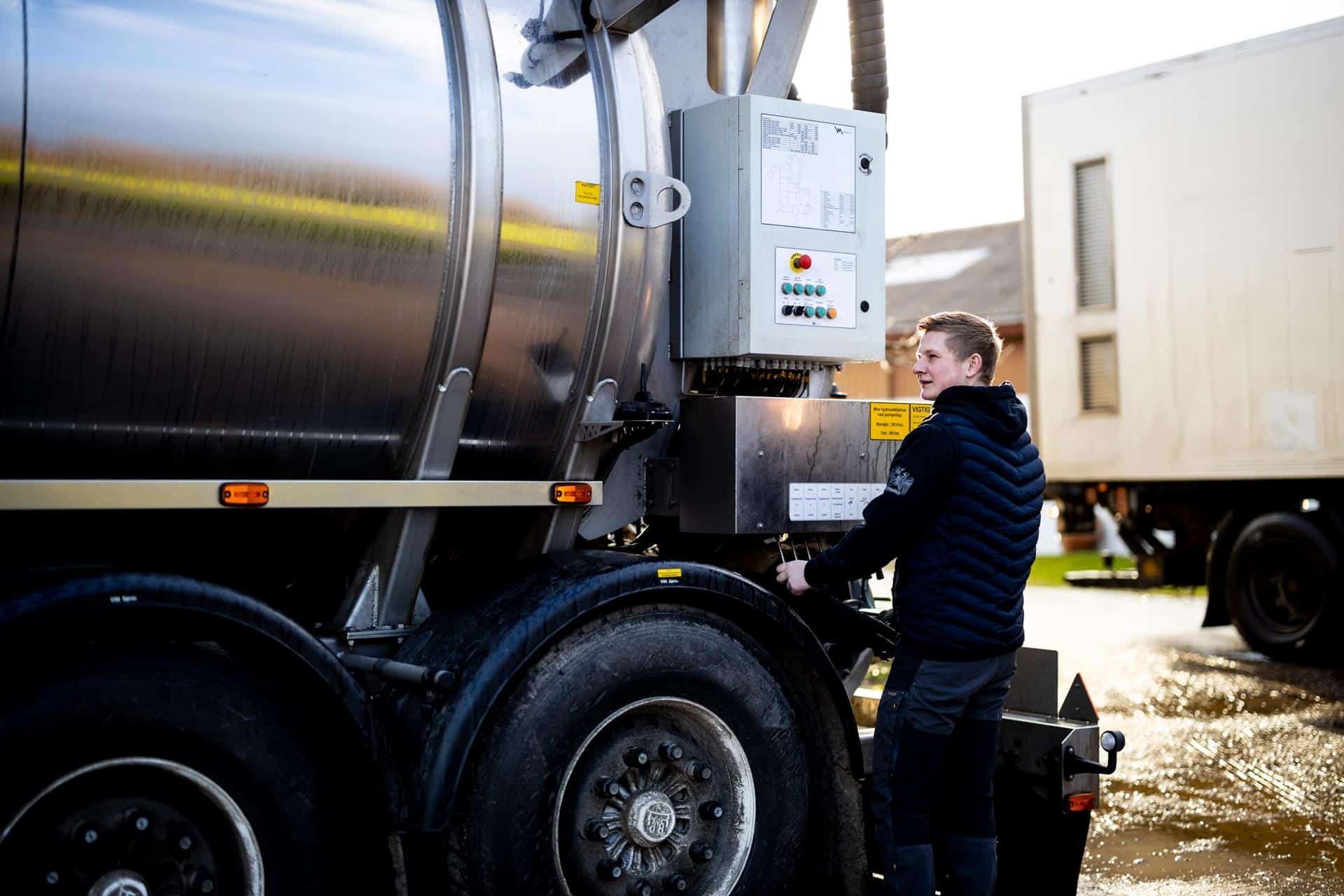 Mandlig medarbejder betjener kontrolpanelet bag på en Gustav Hansen tankvogn.