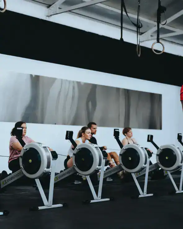 Members working out on rowers with coach
