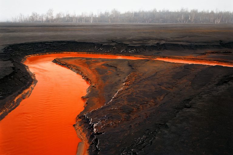 Lava flow in a volcanic landscape with vibrant orange-red hues and dark volcanic terrain.