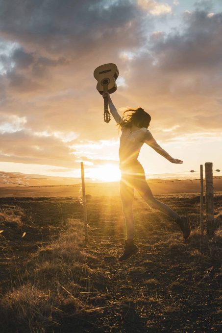 Iceland, woman jumping with guitar at sunset Iceland, woman jumping with guitar at sunset