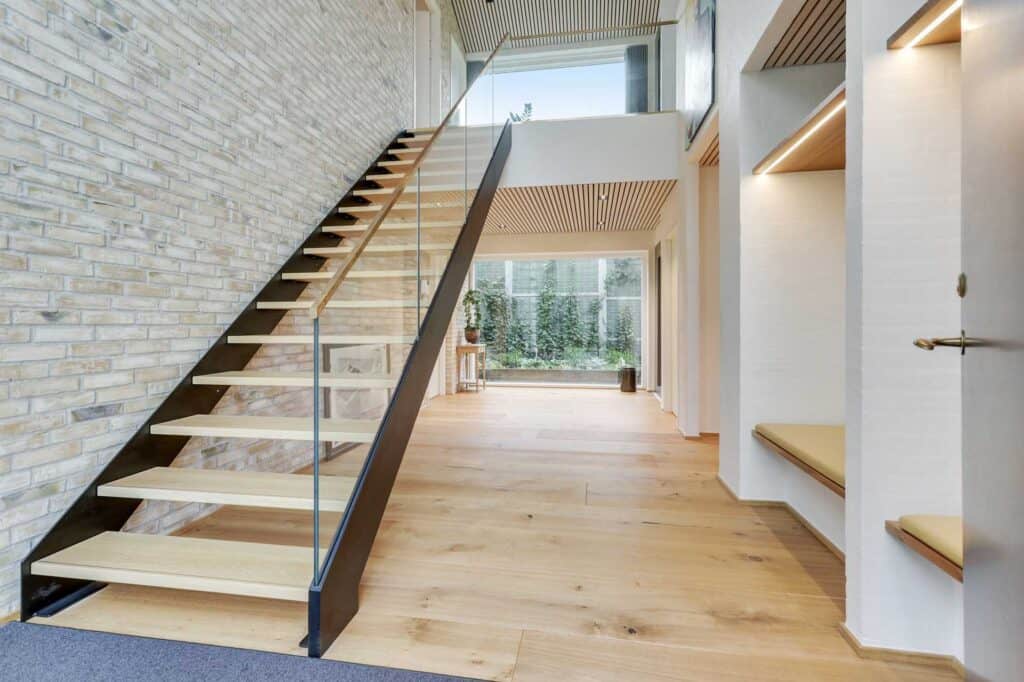 Åben trætrappe i hall med højt til loftet i moderne hus.