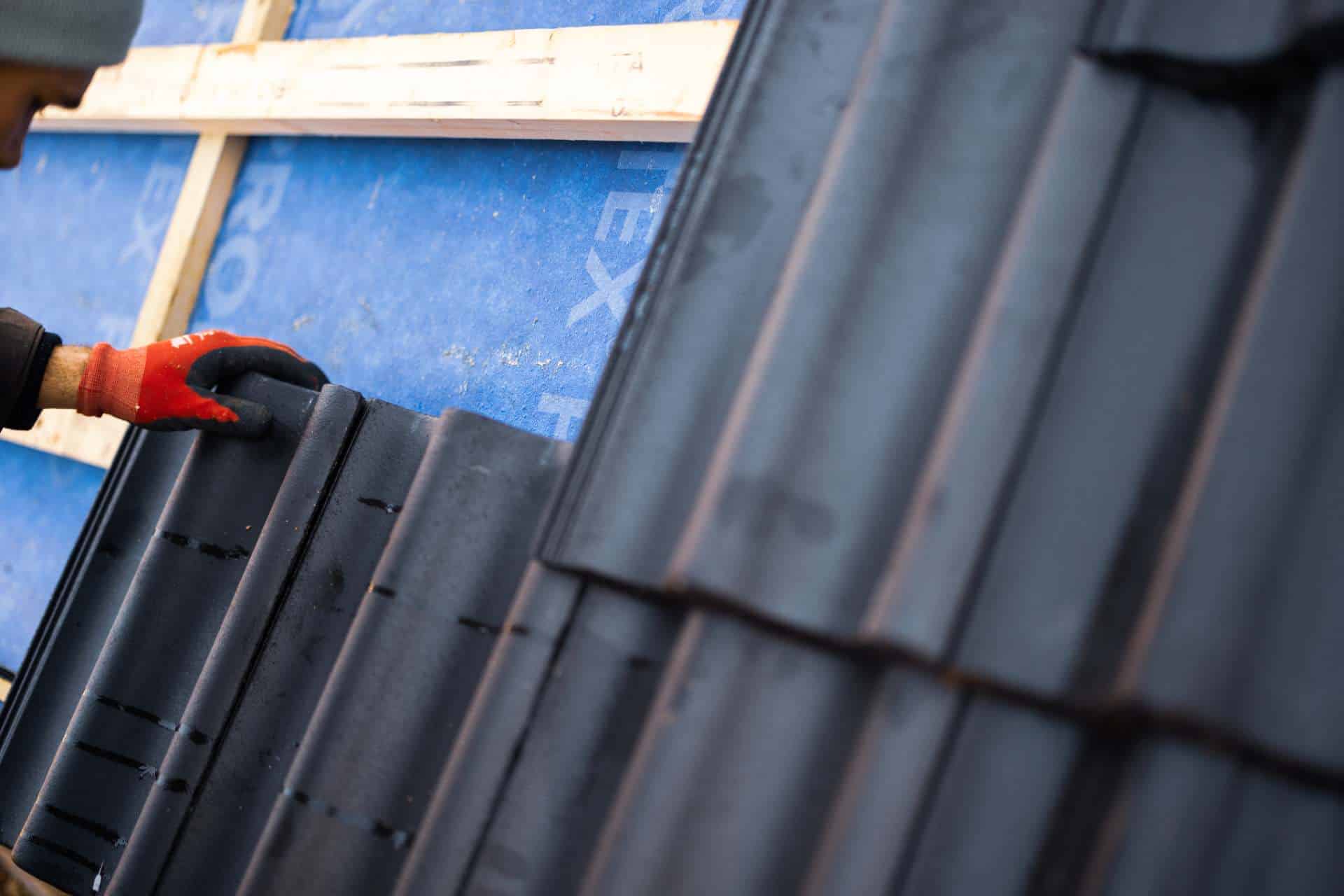 Tømrer i Næstved lægger mørke tagsten på taglægter over blåt undertag