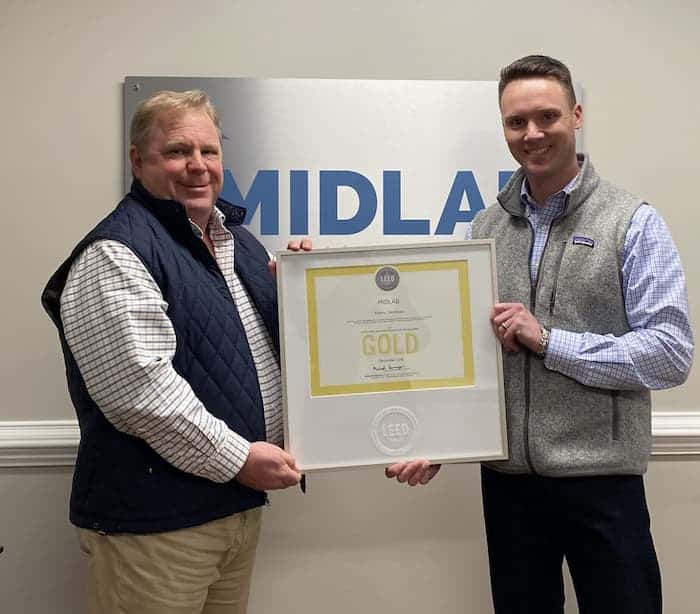Two men holding framed gold award before MIDLAB sign