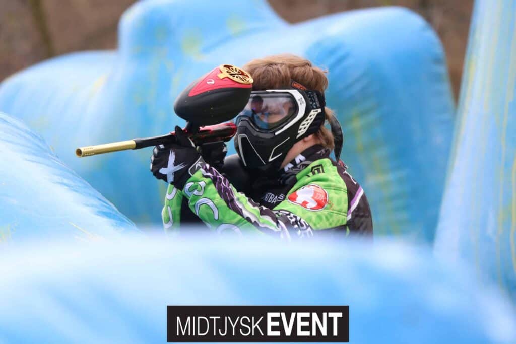 Paintballspiller med grøn trøje gemmer sig bag blå dækninger