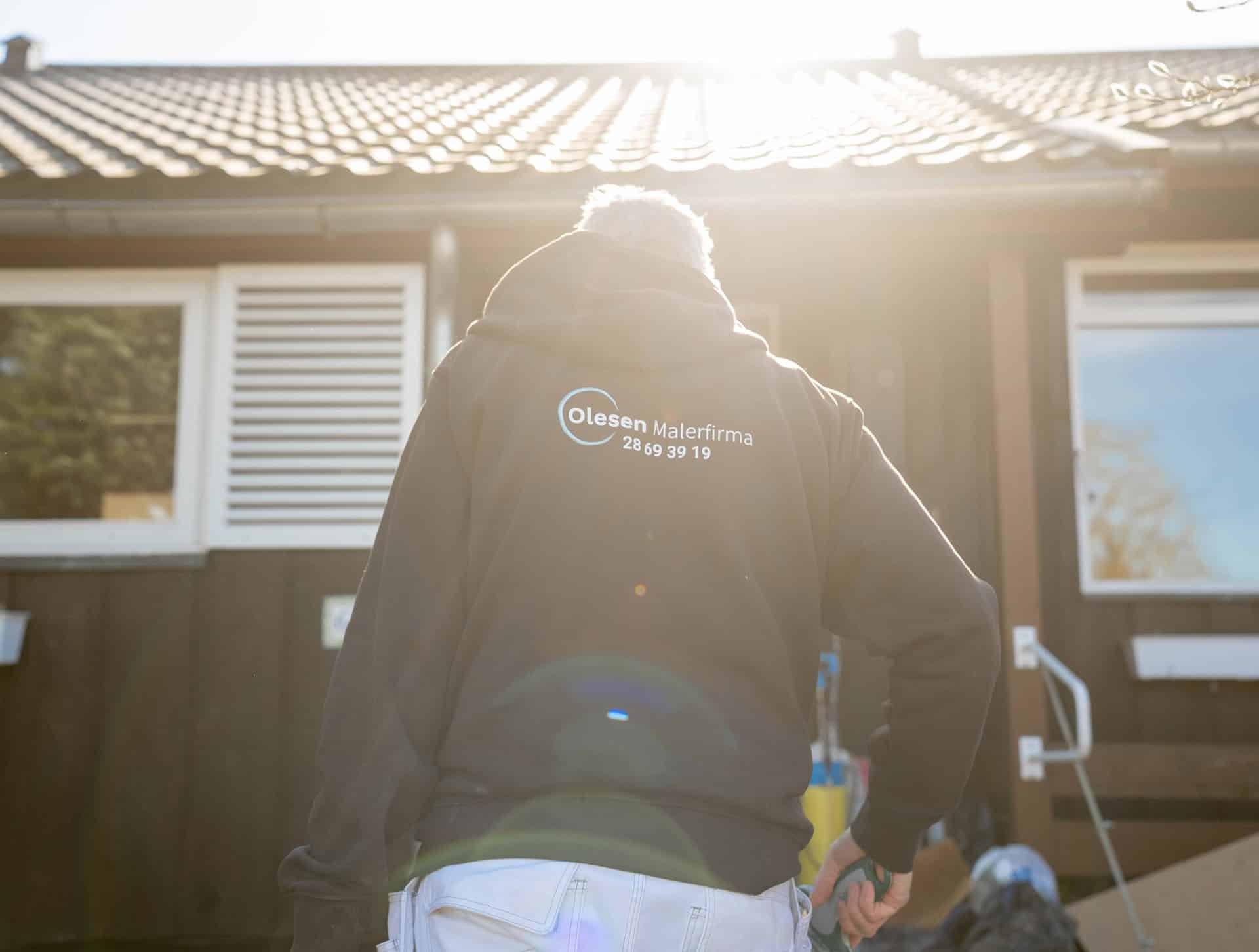 Maler i sort jakke set bagfra under udendørs malerarbejde