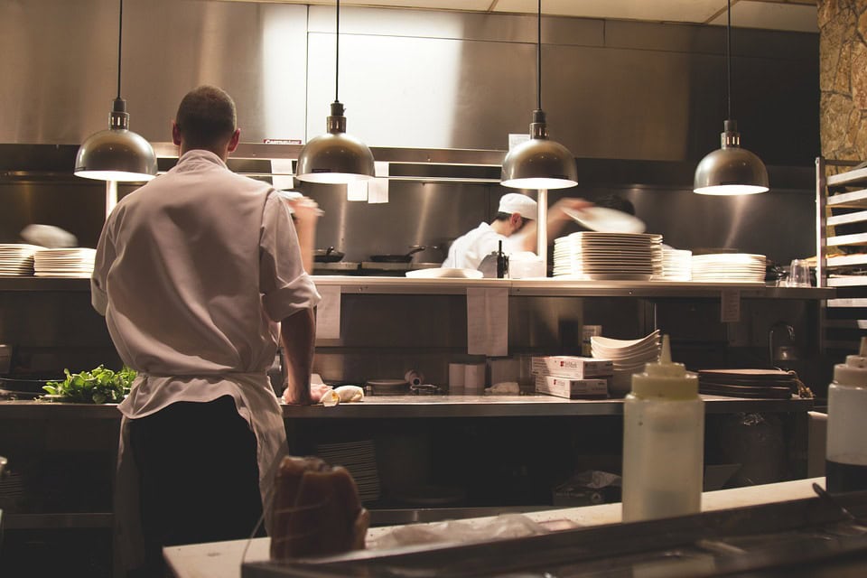 A waiter stands at a busy restaurant pass. You can learn to reduce the water bill at your restaurant with these simple best practices.