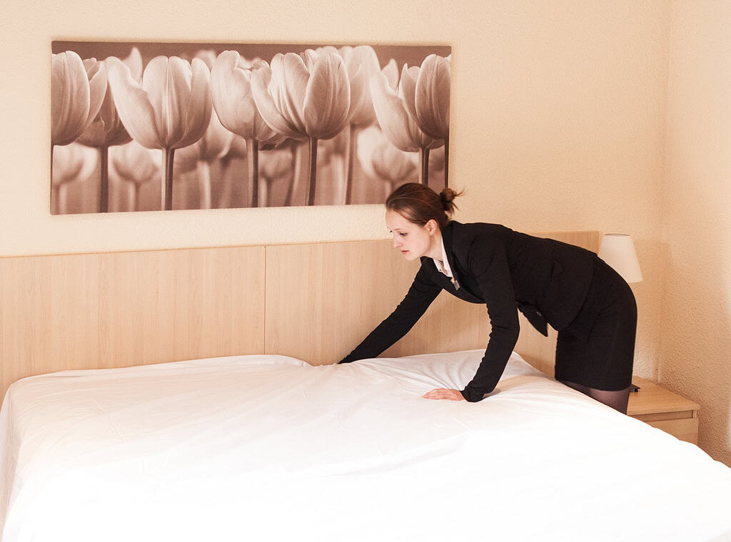 A housekeeper smooths the sheet on a hotel room bed. Use these top hotel housekeeping duties to get positive reviews and repeat business.