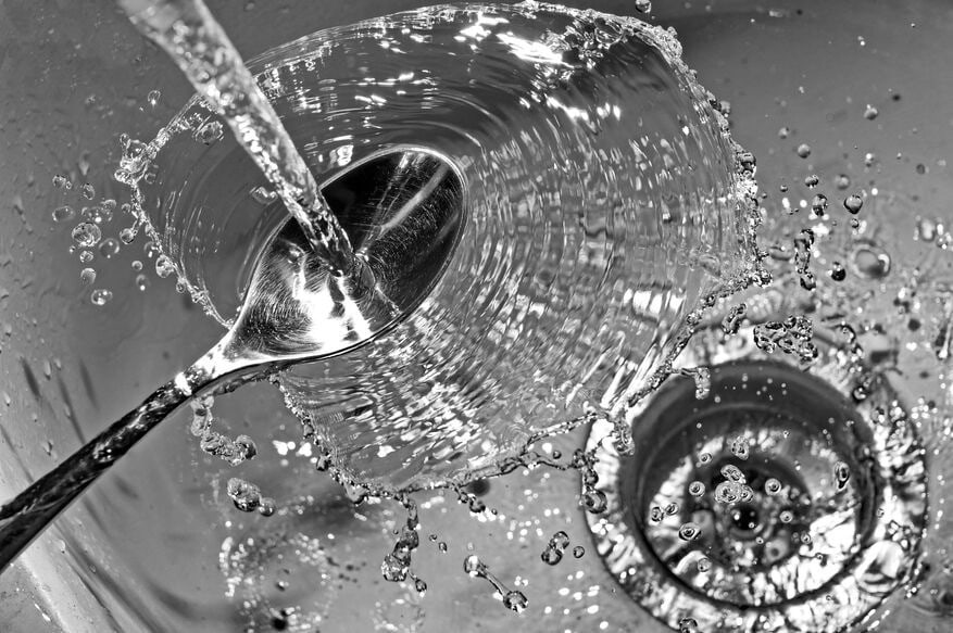 Crystal-clear, soft water pours onto a spoon and into a clean, stainless steel commercial sink.