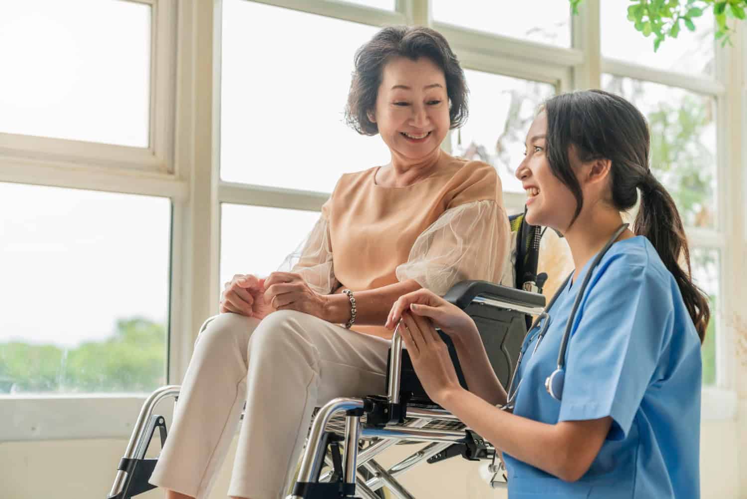 An elderly woman in a wheelchair sits with her caregiver, looking out the window on a bright, sunny day.