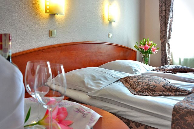 Hotel room bed with two wine glasses and a chilled bottle of wine.