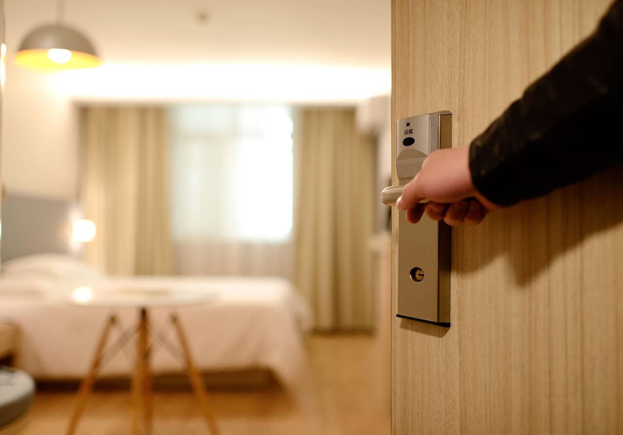 A man's hand opens a door to a clean, contemporary hotel room. Hotels continue to shine in the Airbnb vs. hotel debate.