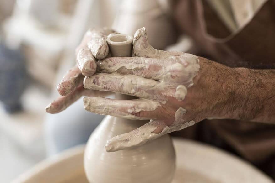A senior citizen’s hands are covered in clay as they use a pottery wheel to craft a vase.