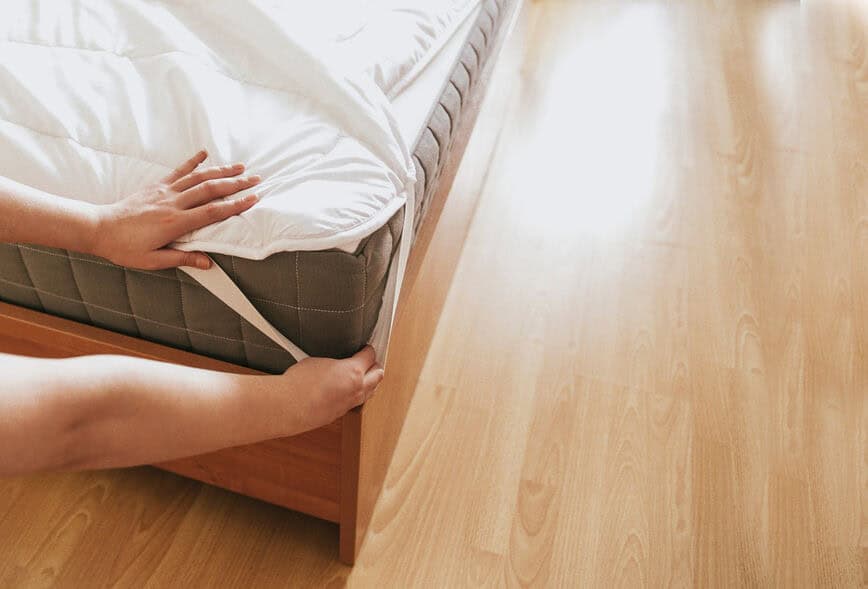 A housekeeper's hands adjust the strap on the bottom sheet of a bed. Hotel housekeeping duties include changing sheets and keeping the room tidy.