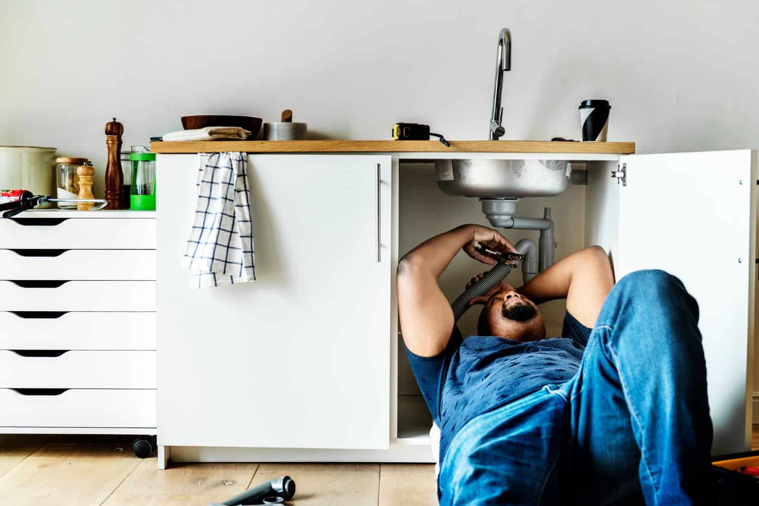 A handyman repairs the pipes under a leaking sink.