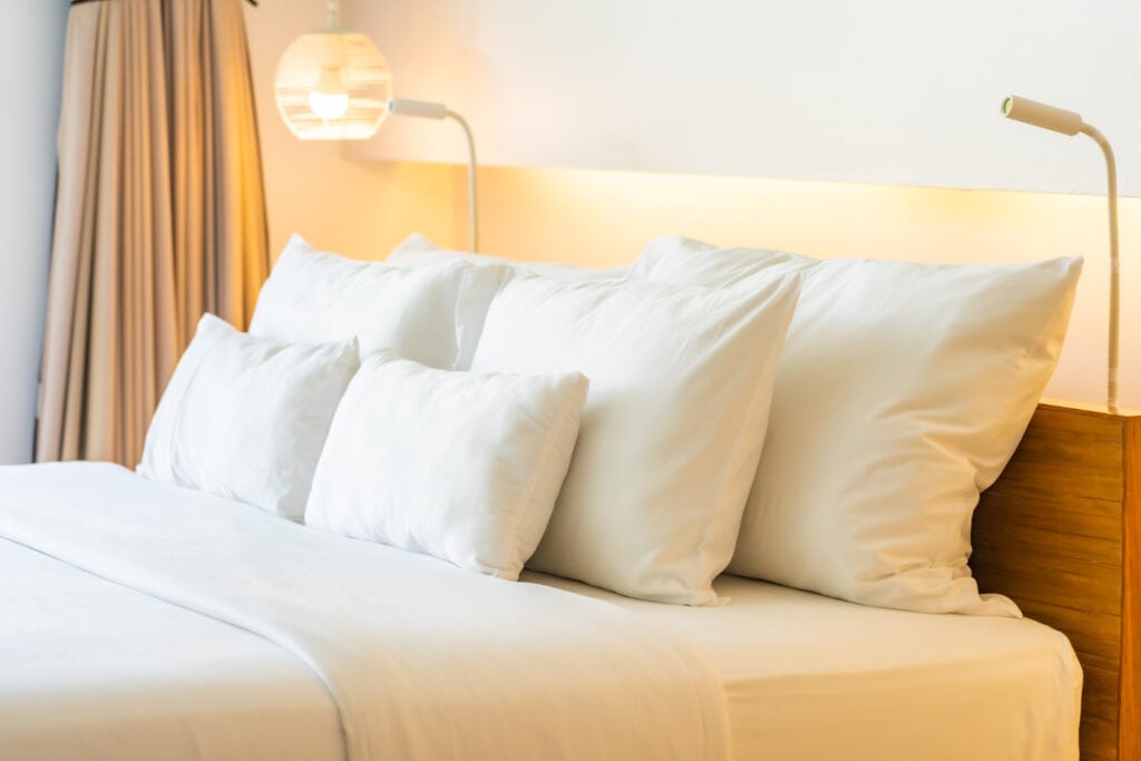 A hotel bed made up with white linens, pillows, and reading lamps on either side of the bed.