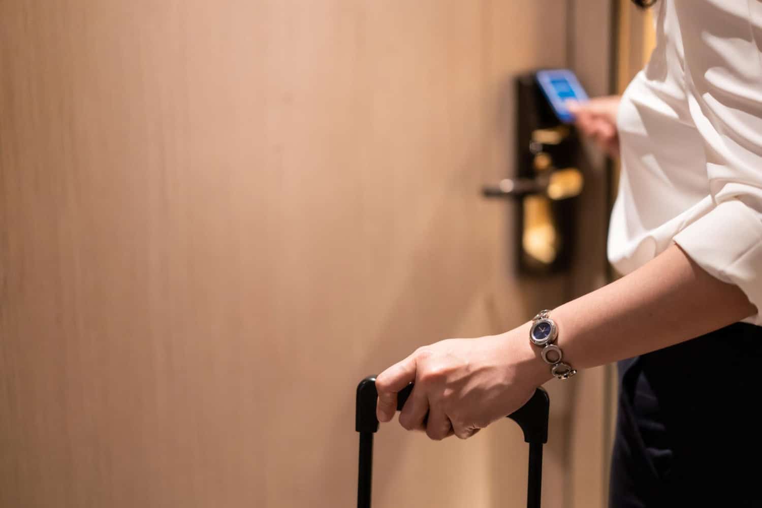 A business woman with a suitcase uses a keycard to enter her hotel room.