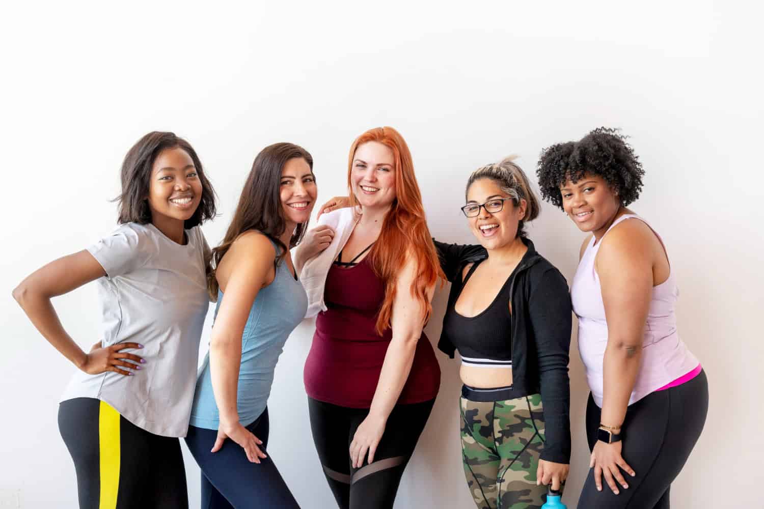 A group of five women in workout clothing, all smiling. The key to gym staff retention is happy staff in a great workplace environment.