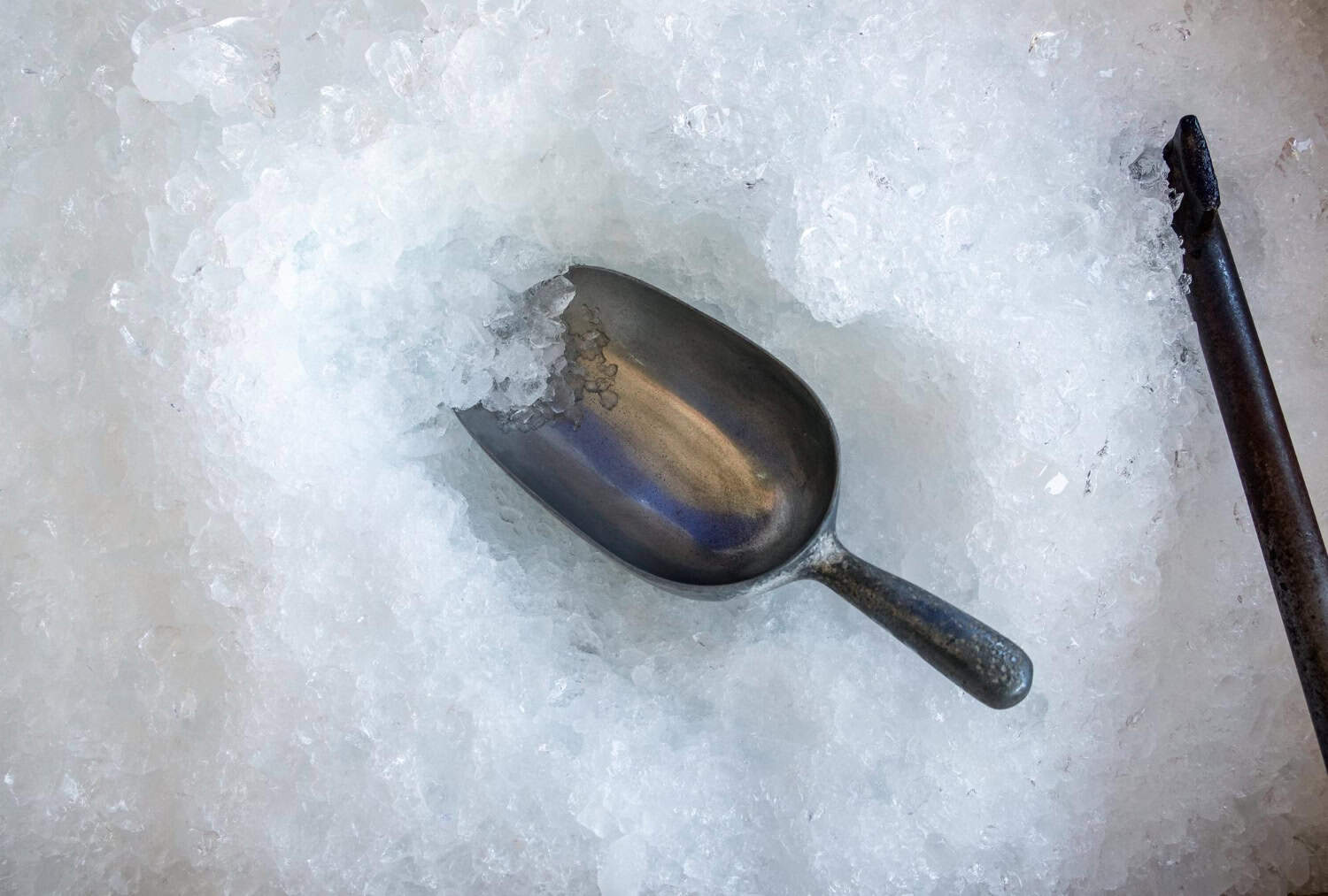 A metal ice scoop sits in a bucket of clear ice cubes.