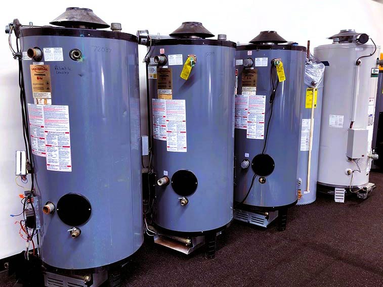 Three large dark grey tank water heaters sit in a warehouse space.