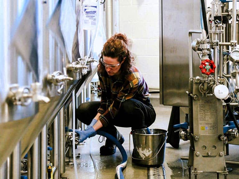 A woman wearing protective eyewear is shown working in a brewery space.