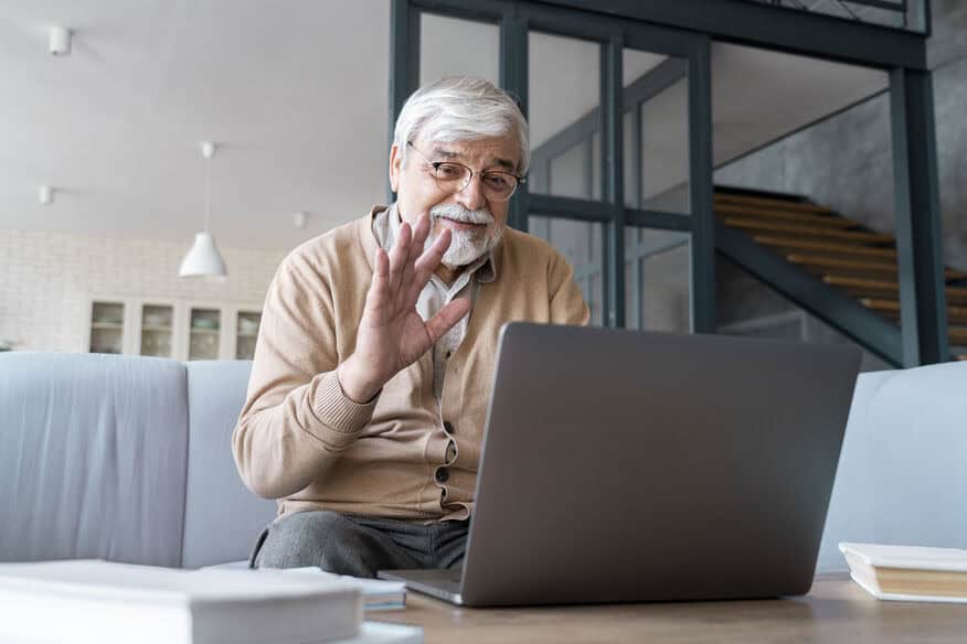 An elderly man waves at an image on his computer. Many senior care lessons were learned during the recent pandemic. 