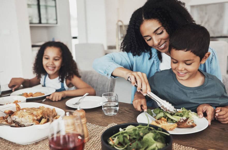 A smiling mom puts salad on her children’s plate. Better frozen food production quality means happier customers.