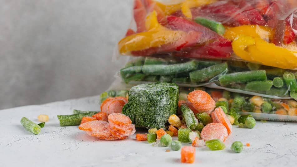 Frozen vegetables spill onto a counter from several bags.