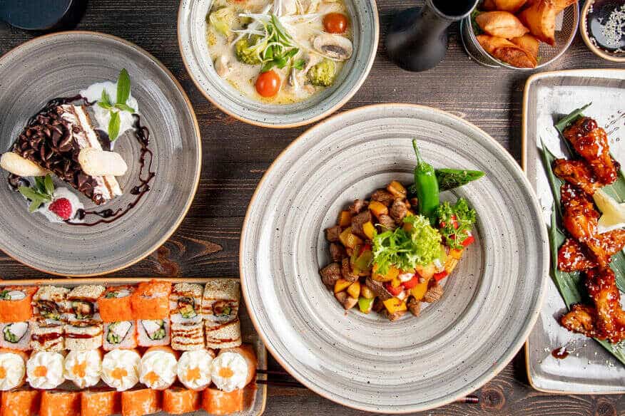 An overhead view of menu options including sushi, cheesecake, steak and potatoes, chicken wings and vegetable soup. If you are learning how to run multiple restaurants, remember you can try something new.