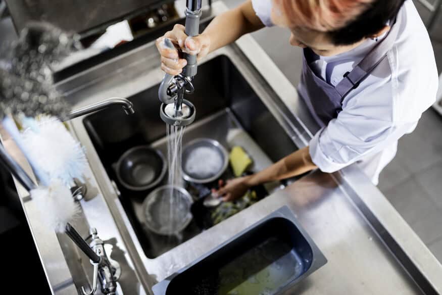 An overhead view of a kitchen employee using a sprayer to rinse dirty dishes in a restaurant.