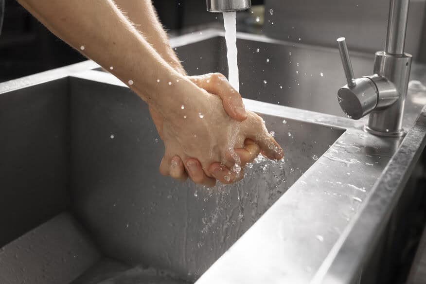 A restaurant employee washes their hands in a stainless-steel kitchen sink with the help of an energy-efficient water heater.