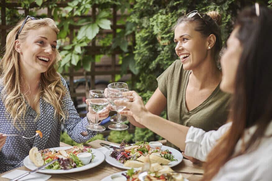 Three women smile and cheer each other as they enjoy a meal at an eco-friendly restaurant.