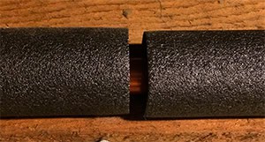 A small piece of pipe is seen through the break in the foam insulation used to reduce commercia water heater energy use.