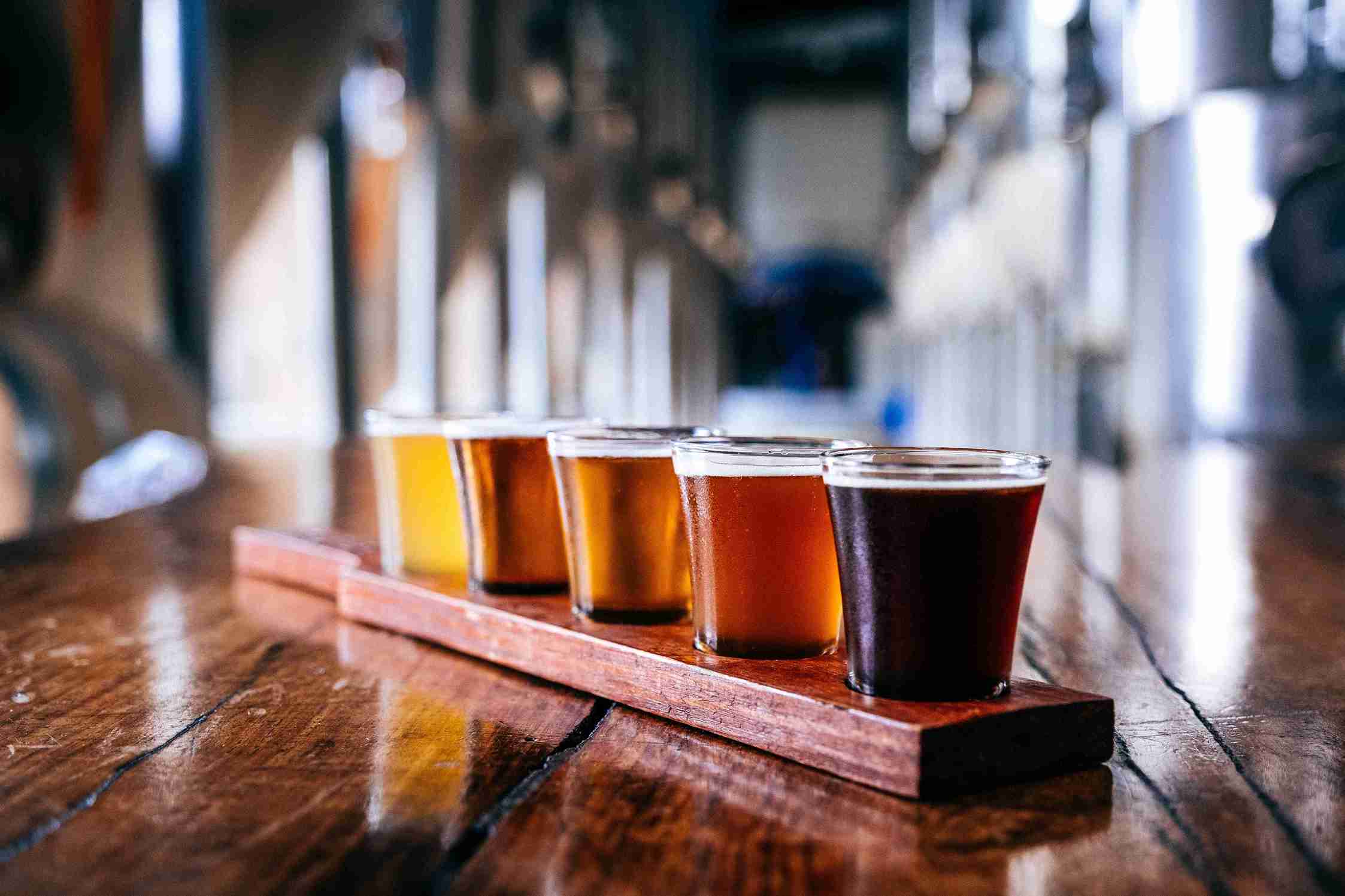 A flight of different colored craft beers on a wooden paddle on a dark wood bar. Successful flavors depend on water softeners for breweries.