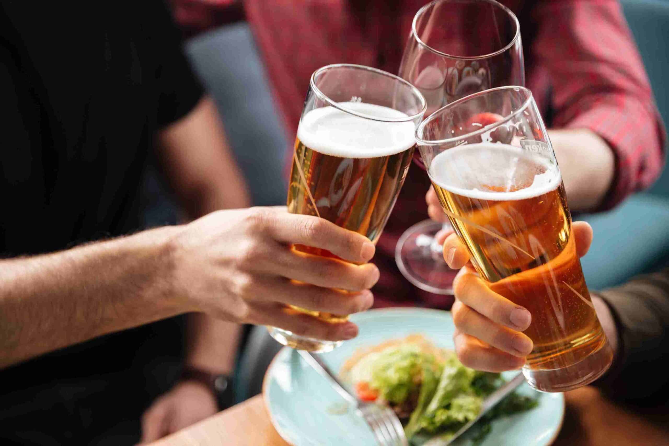 Three friends cheer with beer-filled pint glasses over a table. Water softeners for breweries create flavor profiles you can celebrate.