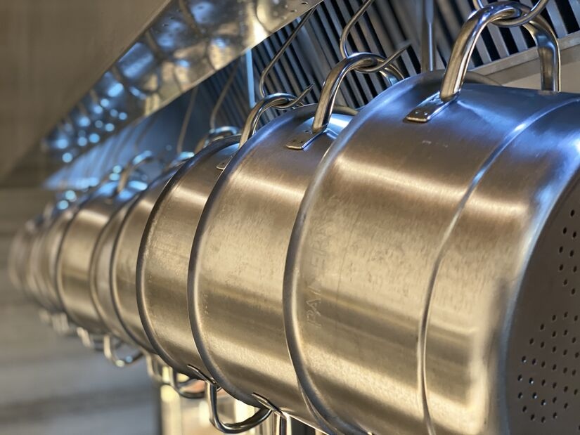 A close-up of a row of hanging stainless steel pots disappearing into the distance of a hotel kitchen. Understanding your hotel's boiler efficiency rating means hot water for all.