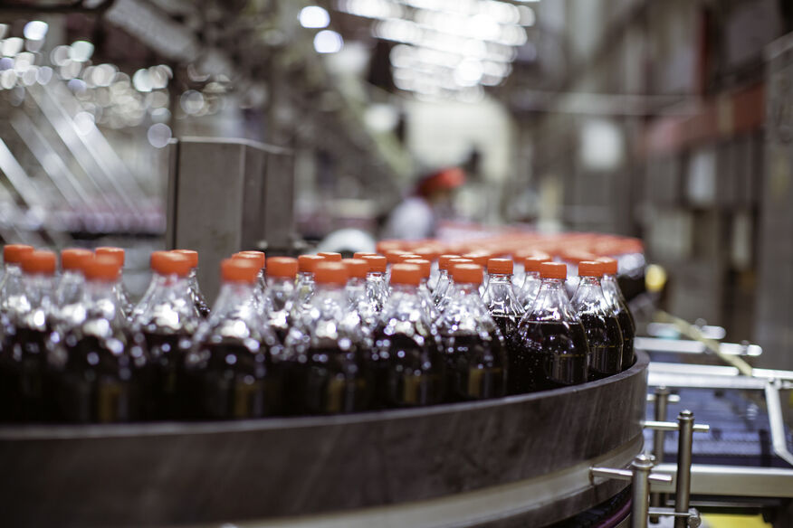 Bottles filled with a dark liquid curve down a conveyor belt using commercial hot water systems that can meet sanitation regulations.