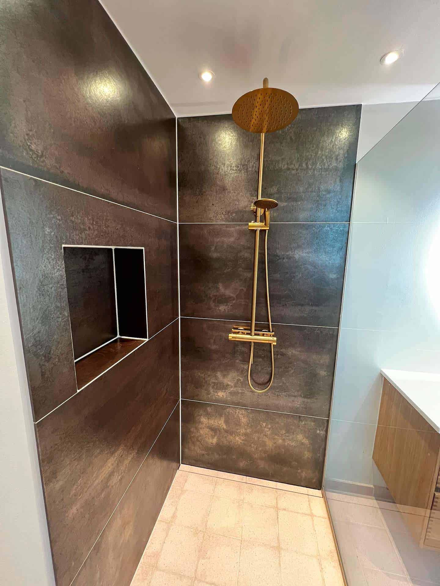 Badeværelsesrenovering med bruser i guld og store fliser på væggen