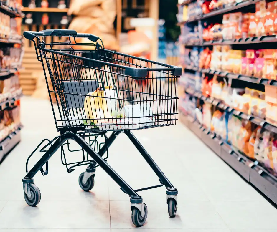 Shopping cart filled with groceries in a supermarket aisle.