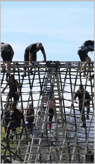 People climbing a wooden obstacle course outdoors during team-building activity.
