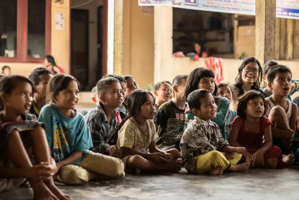 Children sitting on the floor during a community event, engaging in learning activities.