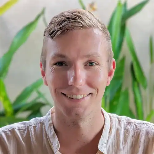 Team member smiling in a professional setting with greenery background.