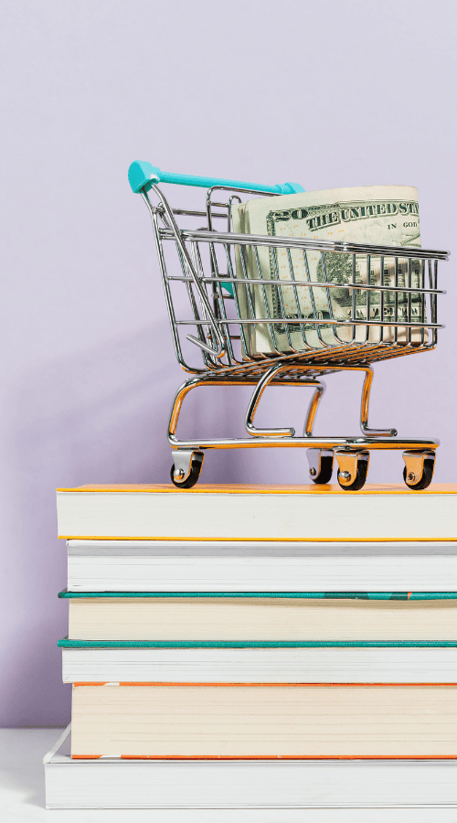 Shopping cart with dollar bills on top of stacked books, representing pricing strategies.