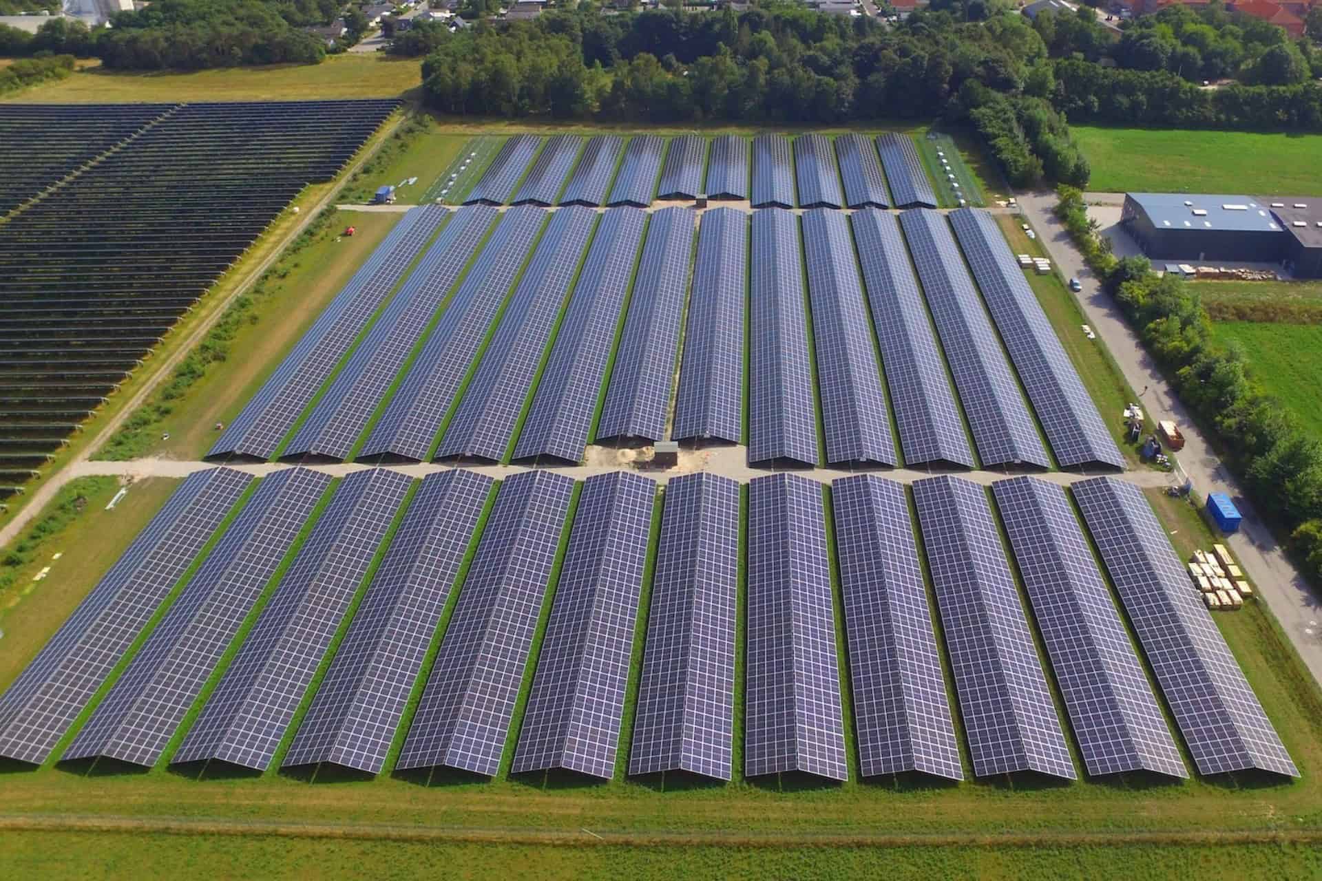 Stort solcelleanlæg med mange solpaneler i grønne omgivelser.