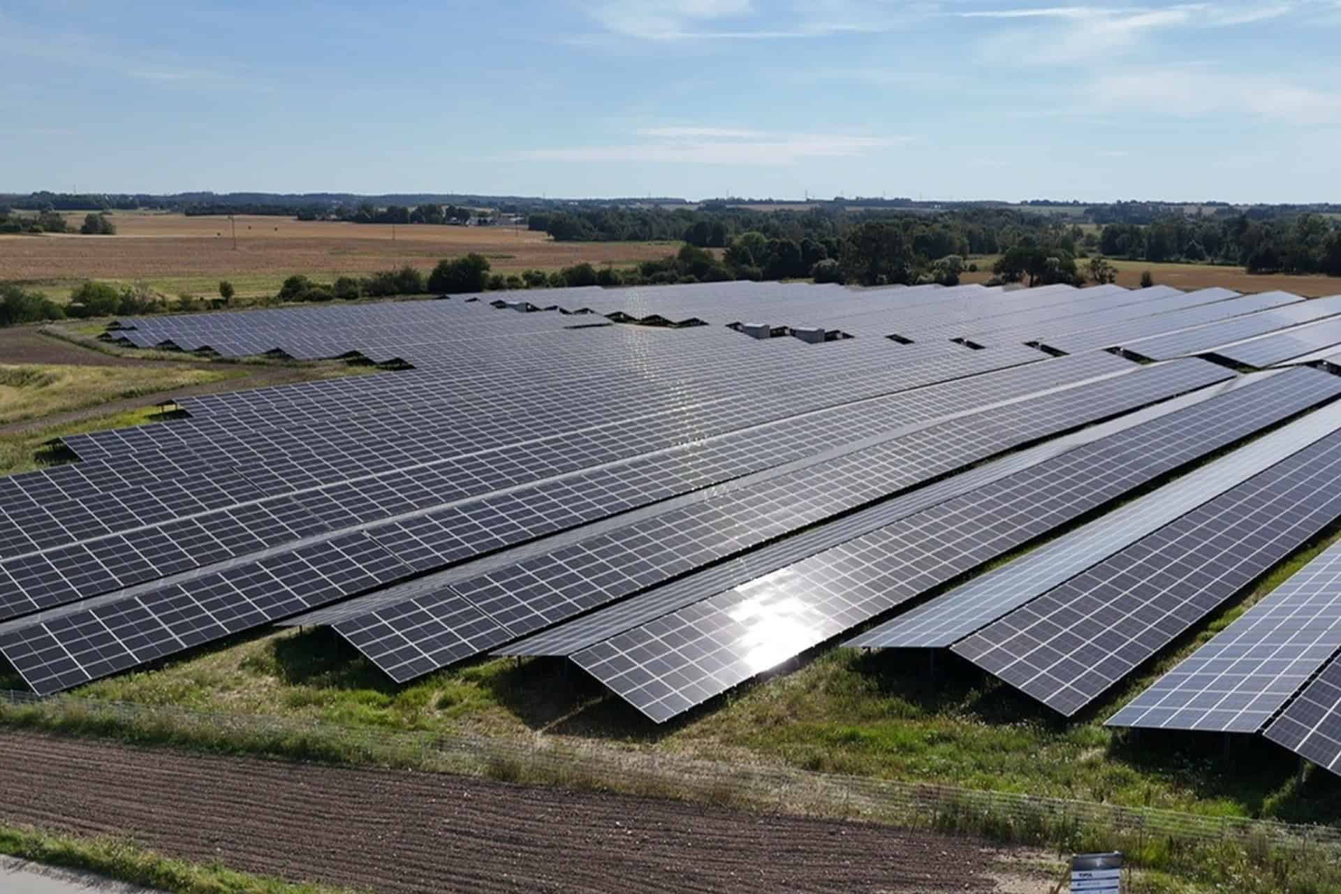 Stort solcelleanlæg i åbent landskab med solrige himmel.