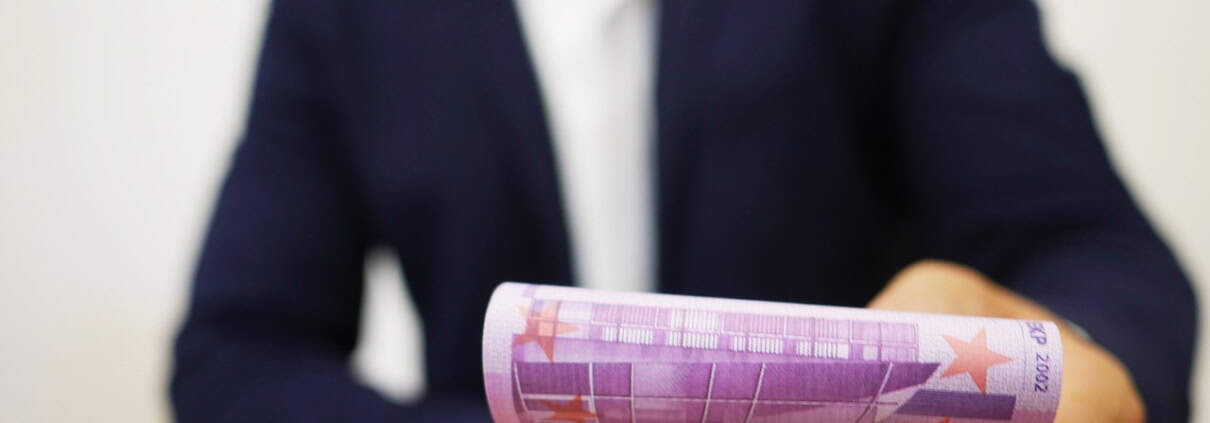 Ondernemer in colbert aan bureau biedt geld aan.