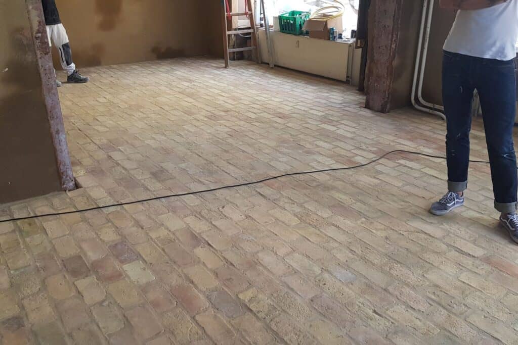 Råt rum med gulv af gule mursten lagt i mønster.