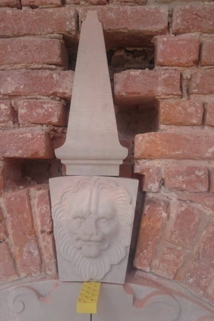 Udskåret stendetalje formet som en lille obelisk på rød murstensbygning.